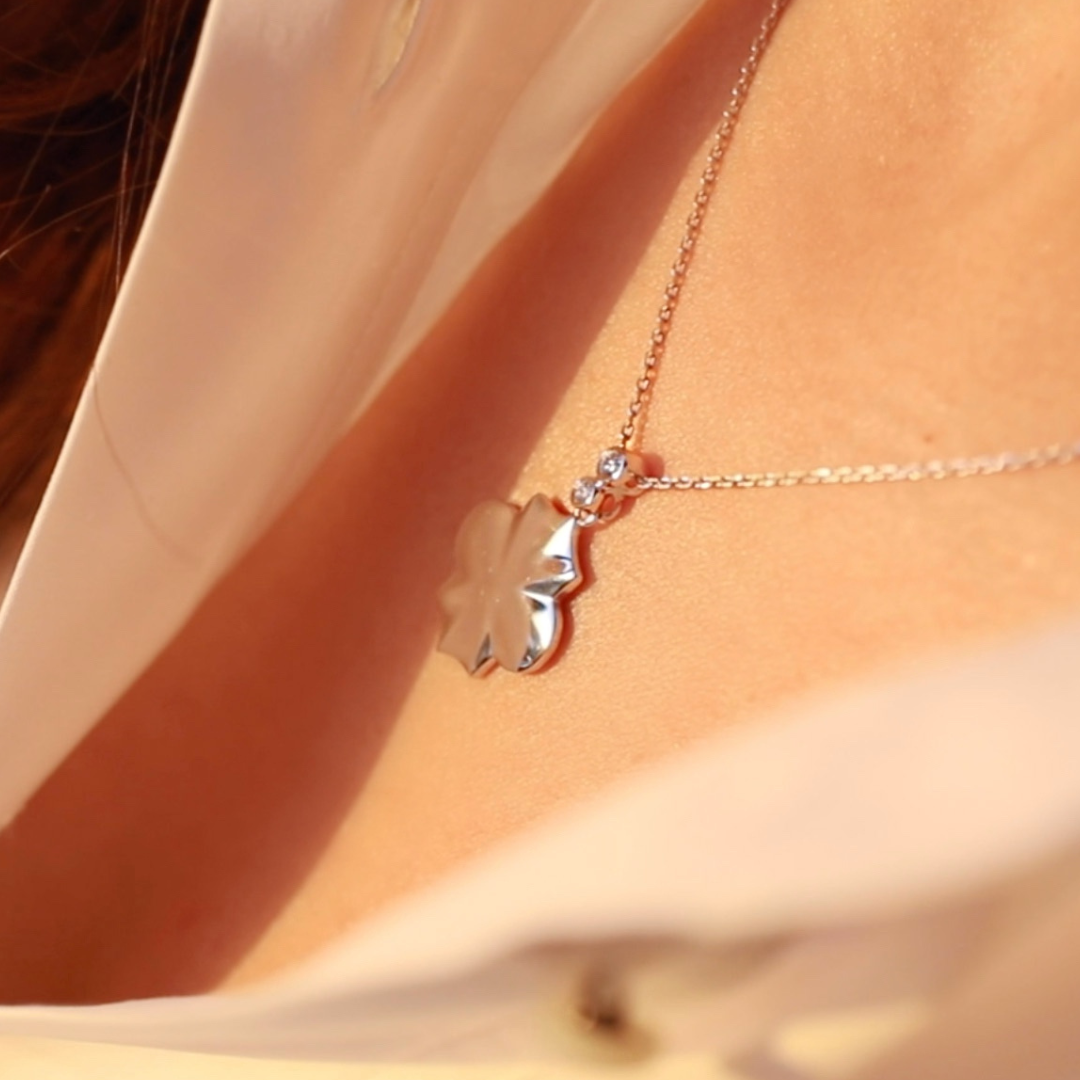 A person wearing a white gold necklace with a geometric shaped pendant.