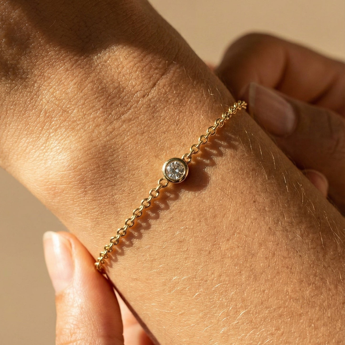 Gold bracelet with a diamond on a wrist against a beige background