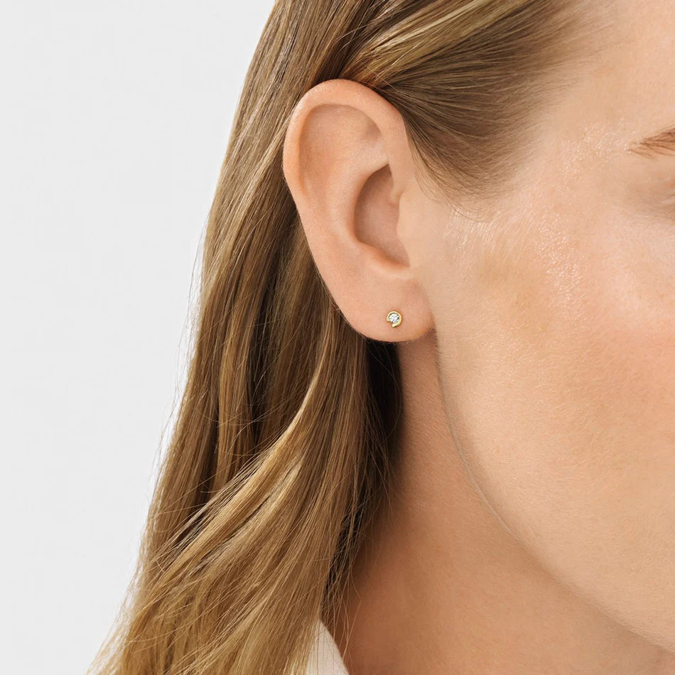 Close-up of a woman's ear wearing a diamond stud earring on a light background
