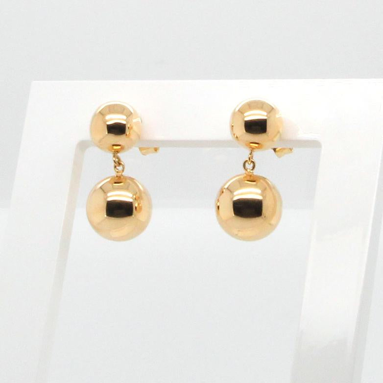 Pair of gold ball earrings on a clear stand against a white background