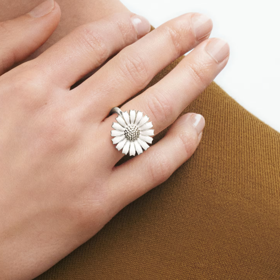 Hand wearing a silver ring with a white flower design on a brown fabric background