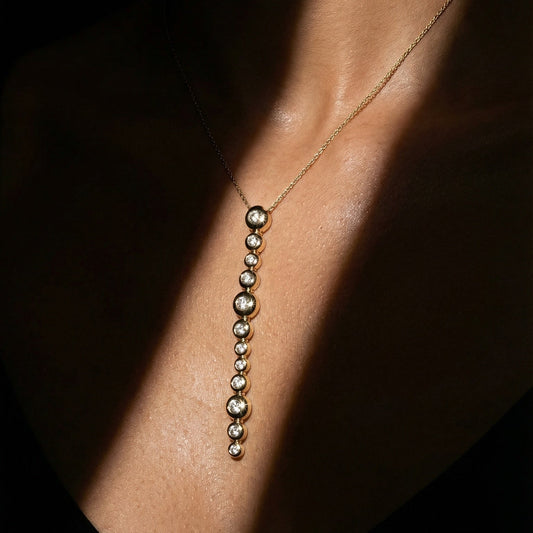 close up of a model in a black suit wearing long drop yellow gold and diamond necklace 