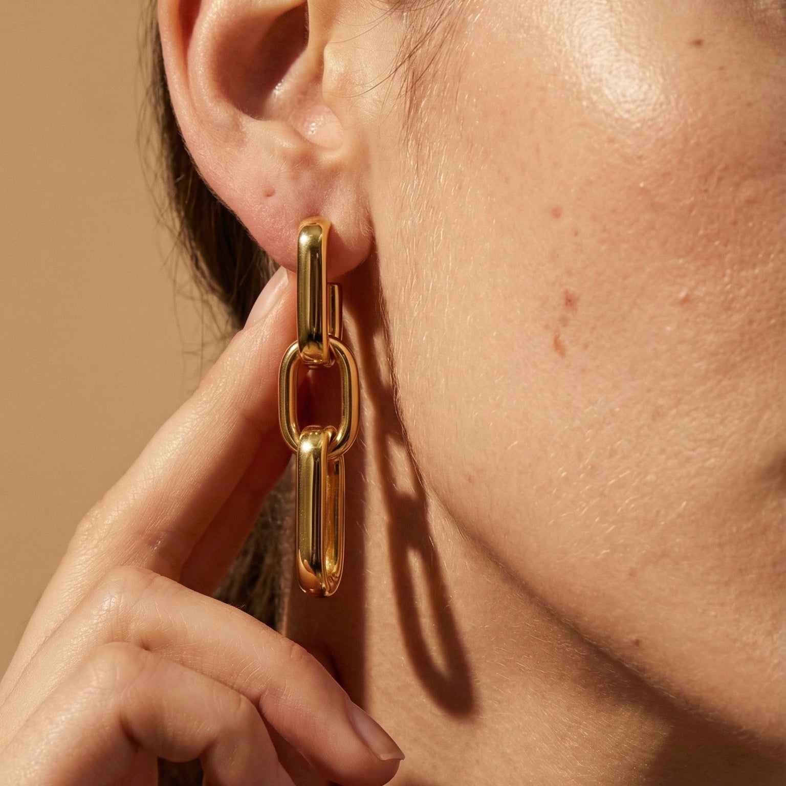 a model wearing 3 chain link drop earrings in yellow gold 