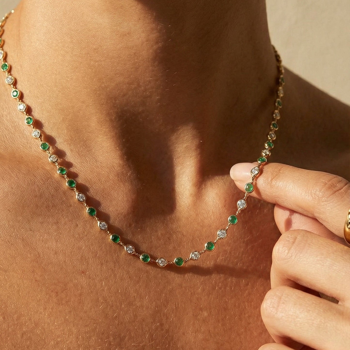 Necklace with green and clear beads being held by a hand on a beige background