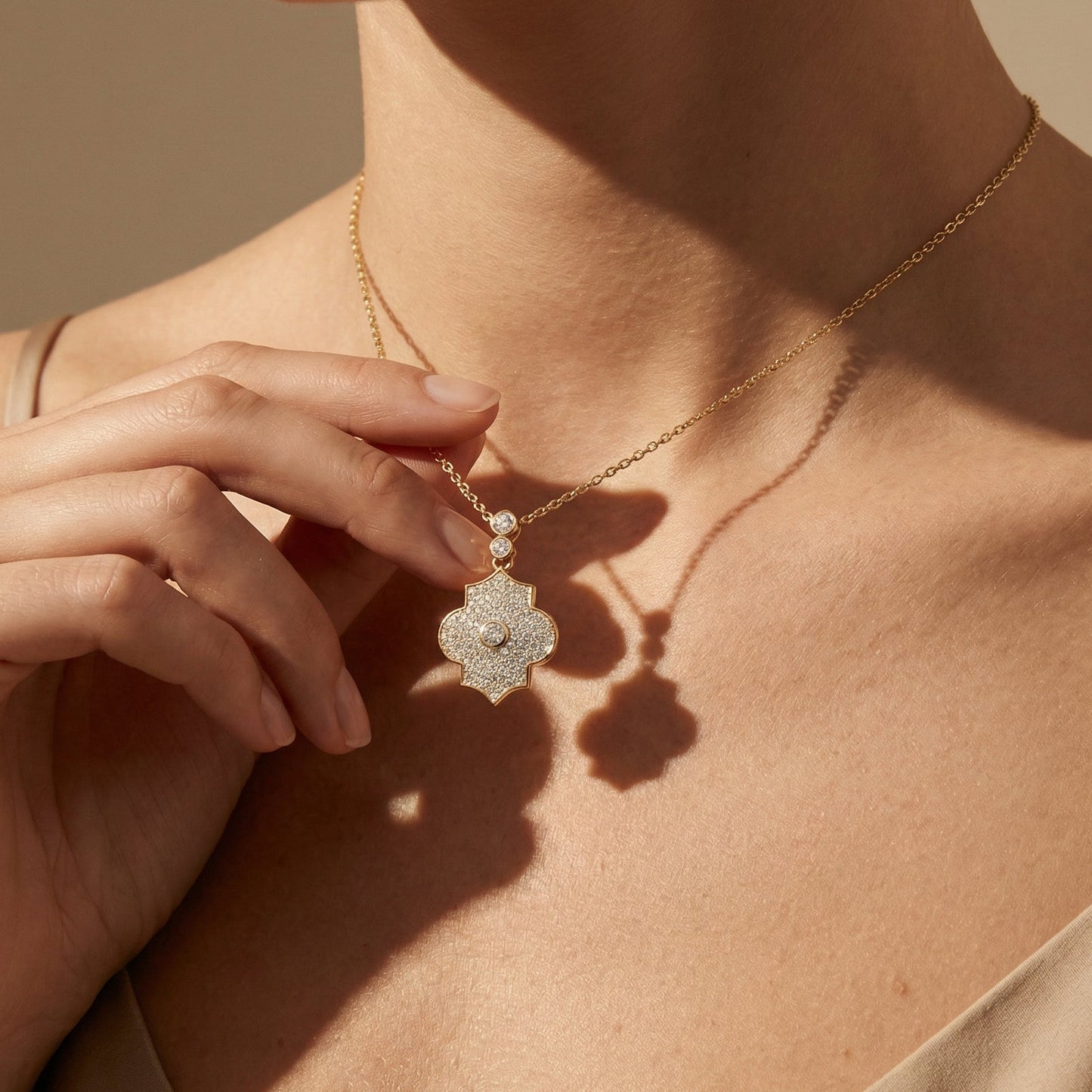 Close-up of a person wearing a gold necklace with a decorative pendant against a neutral background