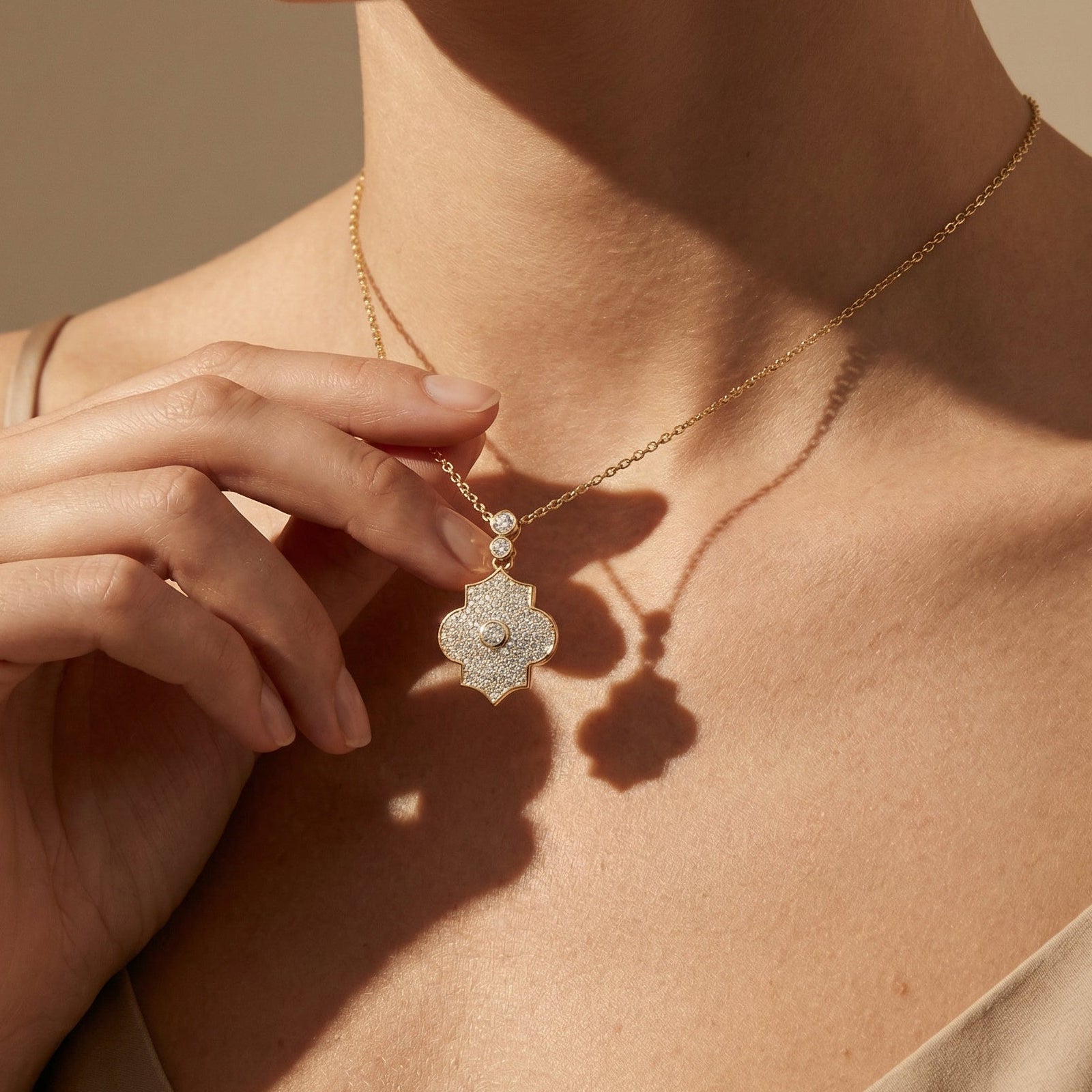 Close-up of a person wearing a gold necklace with a decorative pendant against a neutral background