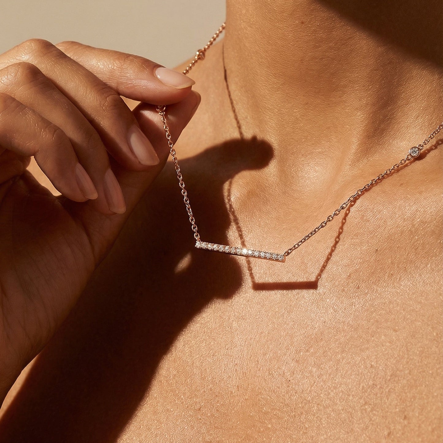 Close-up of a person wearing a delicate necklace against a neutral background