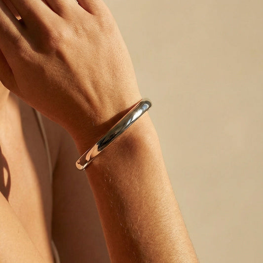 Close-up of a person wearing a gold bracelet on a beige background