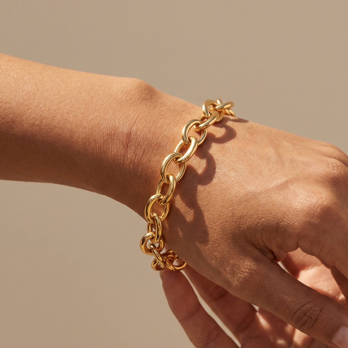 Gold chain bracelet on a wrist against a beige background