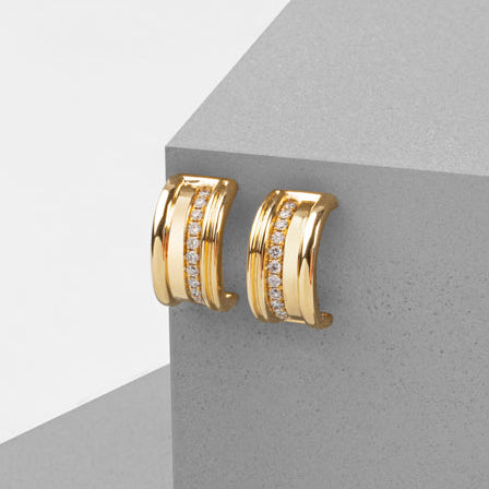 Gold hoop earrings with embedded stones on a gray surface