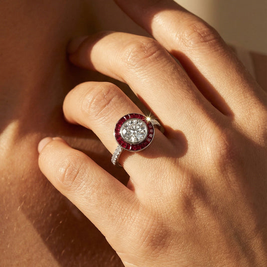 Close-up of a hand wearing a ring with a red gemstone on a neutral background