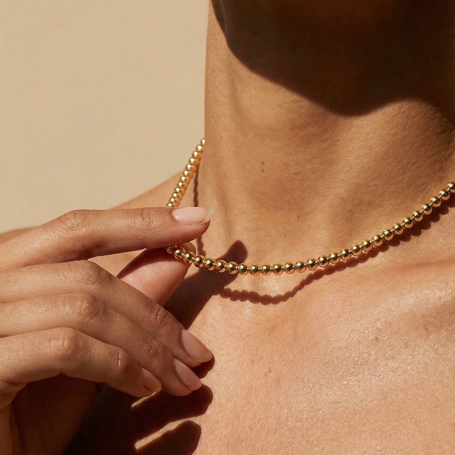 Close-up of a person wearing a gold necklace against a beige background