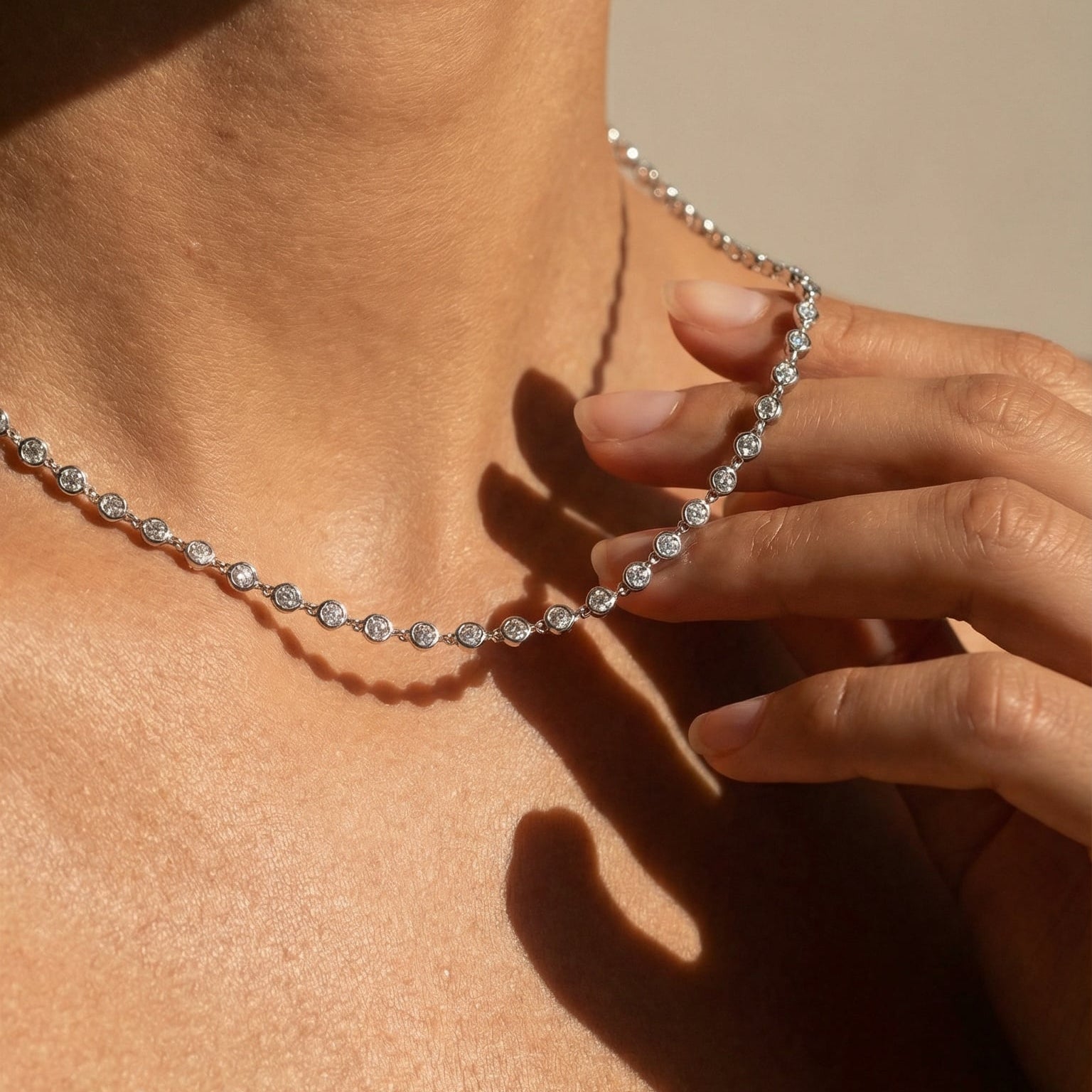 Close-up of a person wearing a silver necklace with a neutral background