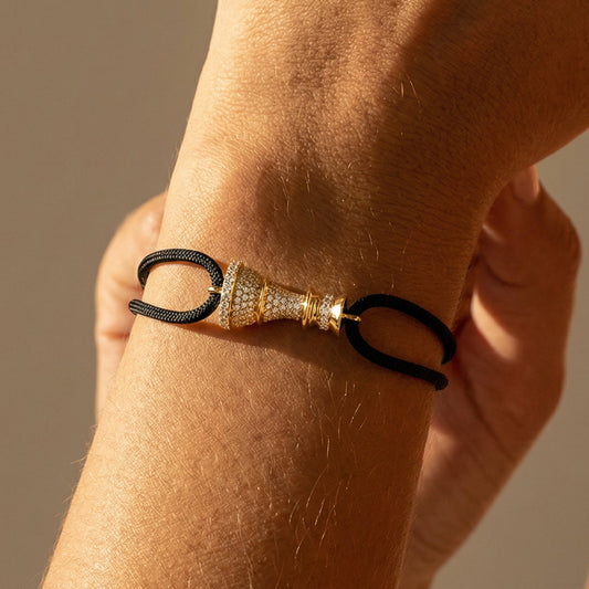 Close-up of a wrist wearing a full diamond chess queen bracelet on a black cord  with a neutral background