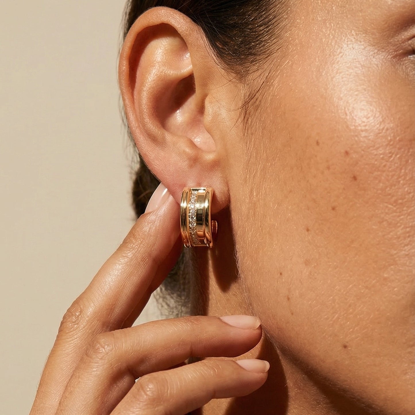 Close-up of a person wearing gold hoop earrings with a neutral background