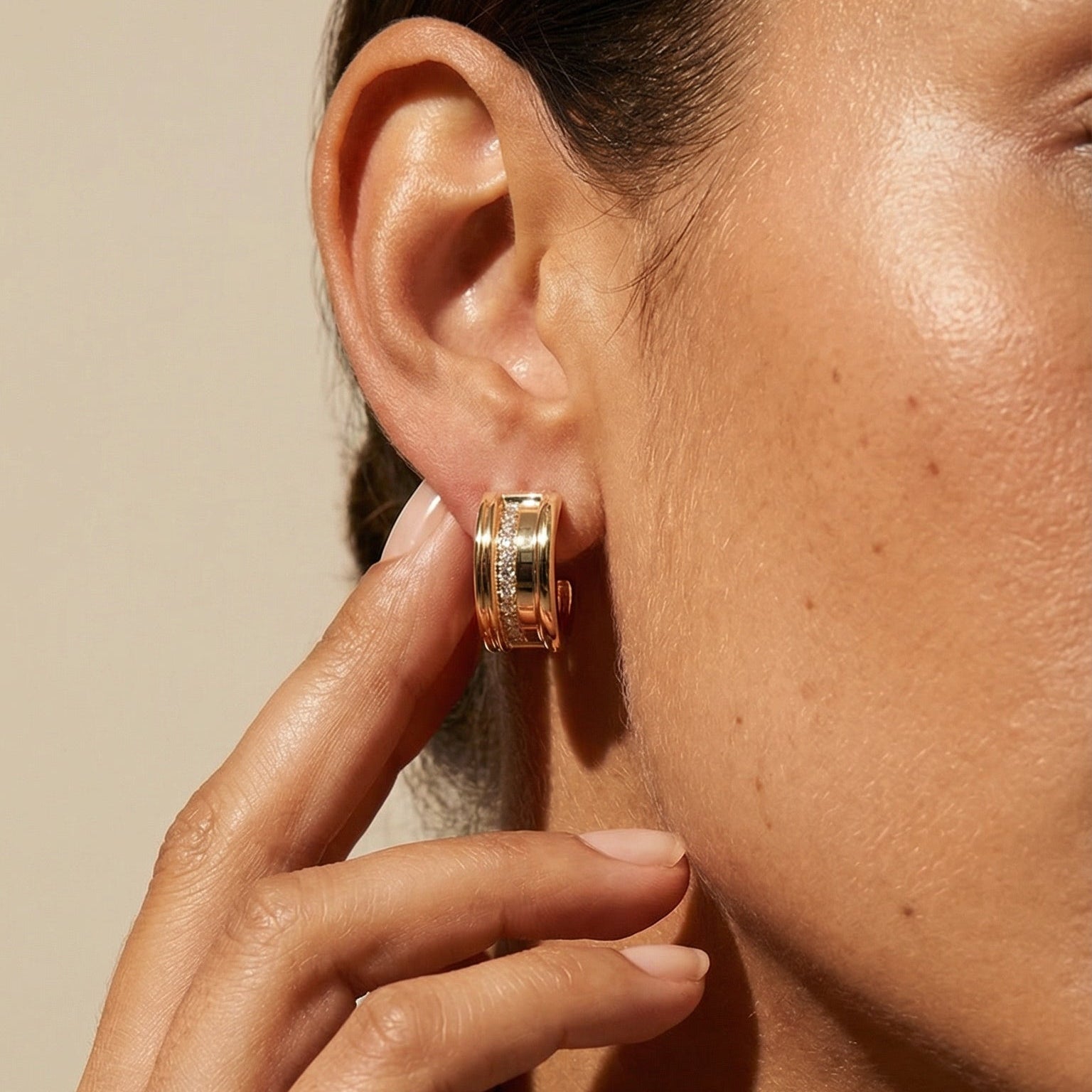 Close-up of a person wearing gold hoop earrings with a neutral background