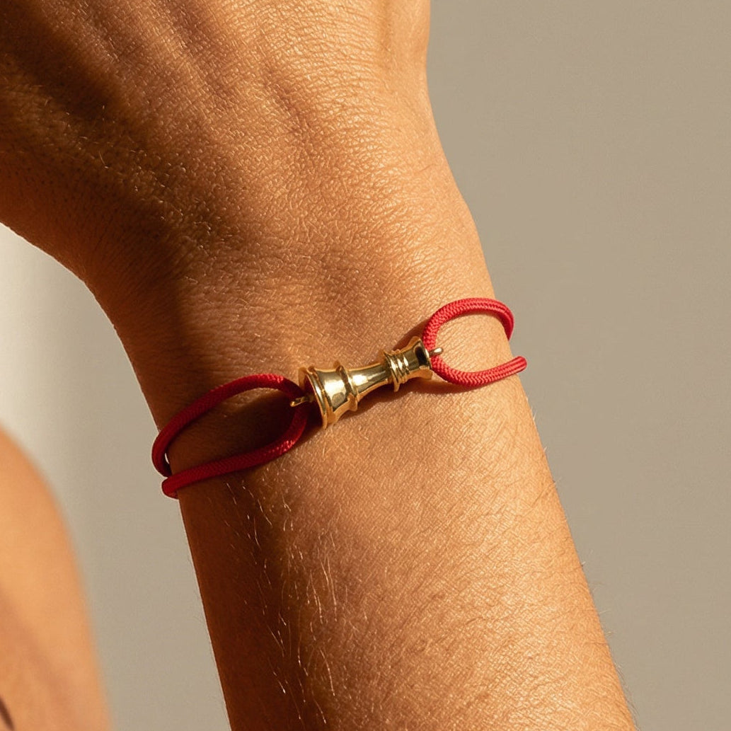 Close-up of a person wearing a red bracelet with a gold chess queen charm on a neutral background