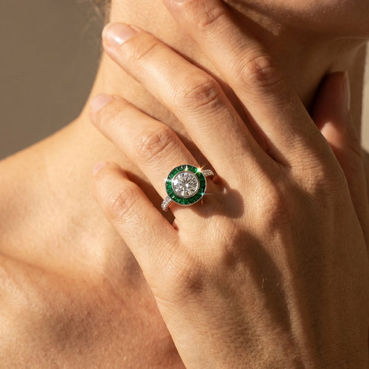 Close-up of a hand wearing a green gemstone ring against a neutral background