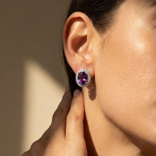 Close-up of a person wearing a purple gemstone earring with a neutral background