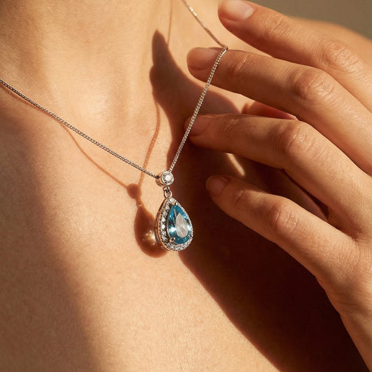 Necklace with a blue pendant being worn, held by a hand against a neutral background