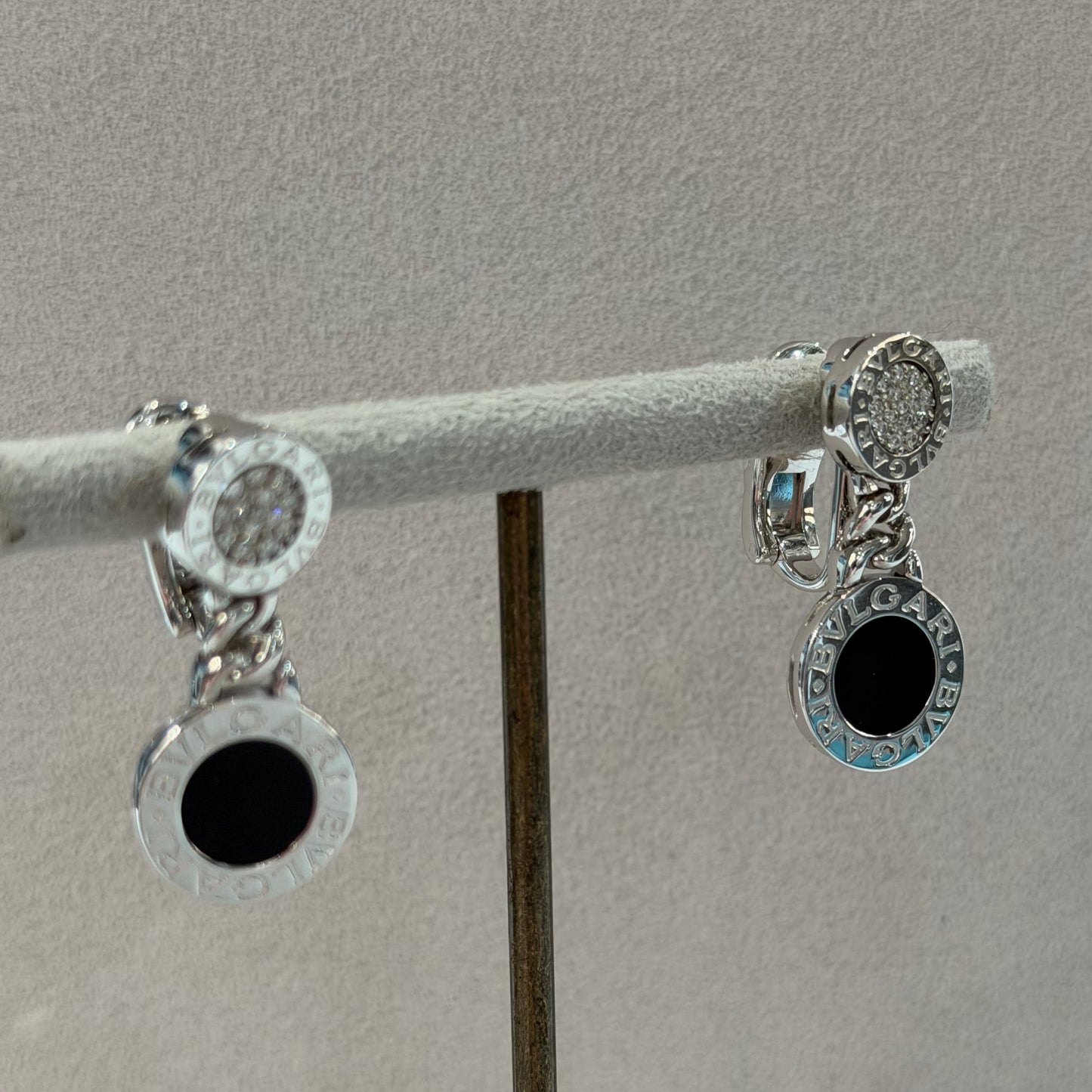 A pair of silver-toned circular earrings with clear stones and black center accents, displayed on a white jewelry stand against a light gray background.