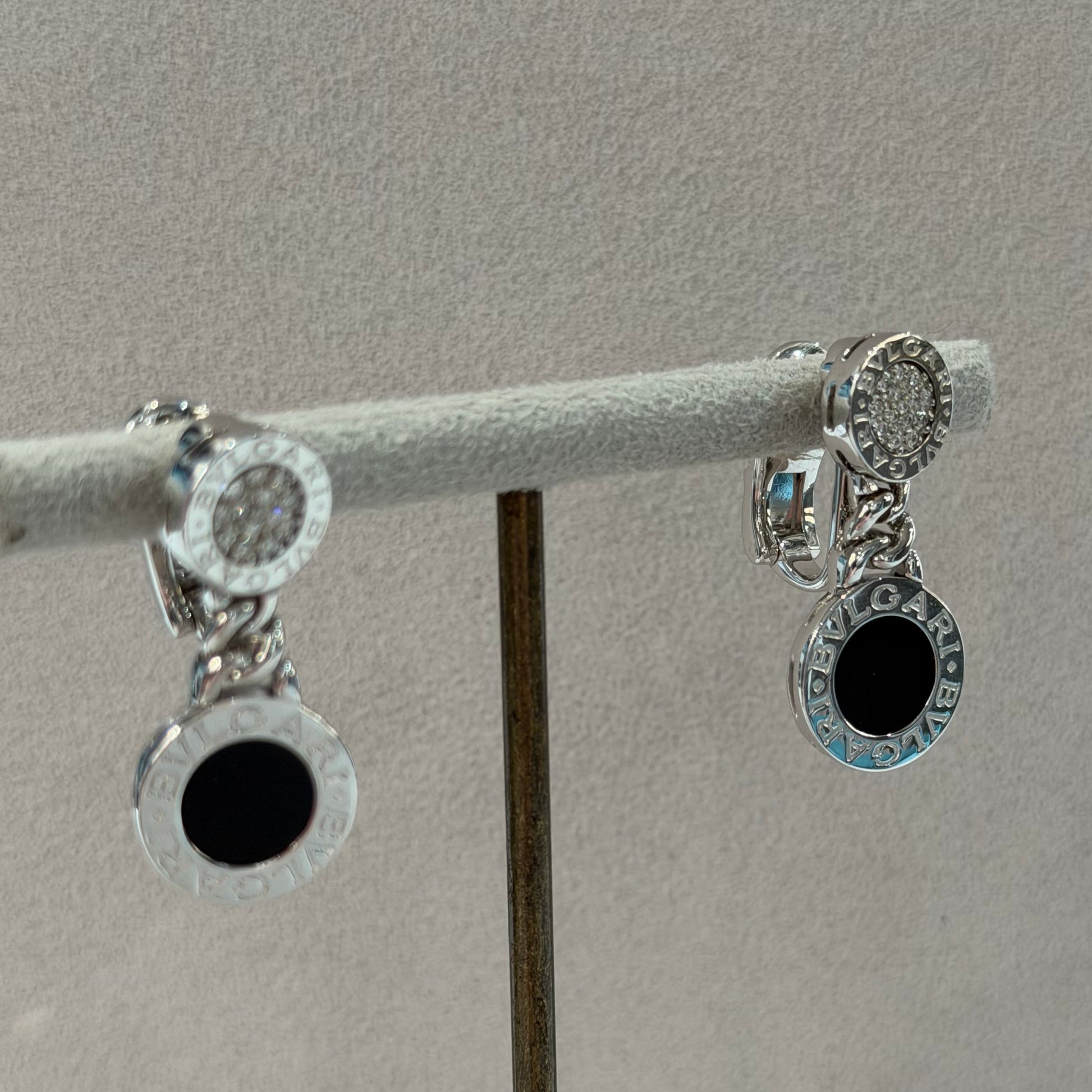 A pair of silver-toned circular earrings with clear stones and black center accents, displayed on a white jewelry stand against a light gray background.