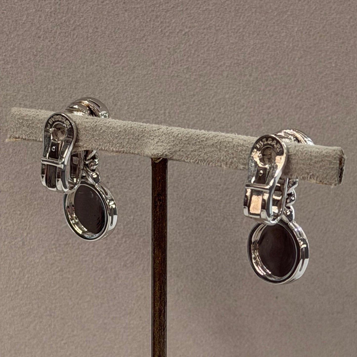 Two silver-toned metal claw settings holding a light gray textured ring display card, suspended against a plain taupe-gray background.