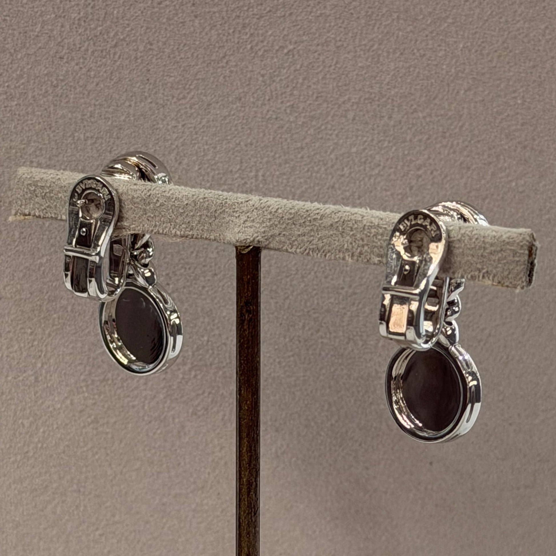 Two silver-toned metal claw settings holding a light gray textured ring display card, suspended against a plain taupe-gray background.