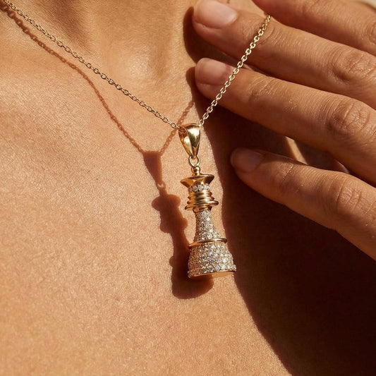 Close-up of a person wearing a chess queen gold and diamond necklace with a pendant against a beige background