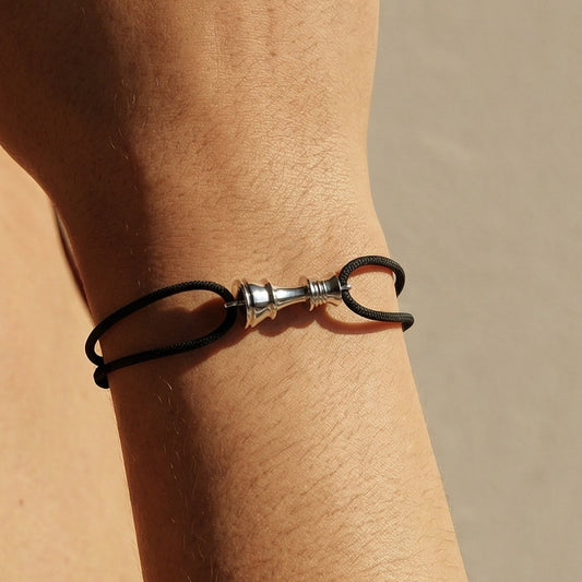 Close-up of a hand wearing a chess queen bracelet on a cord with a neutral background