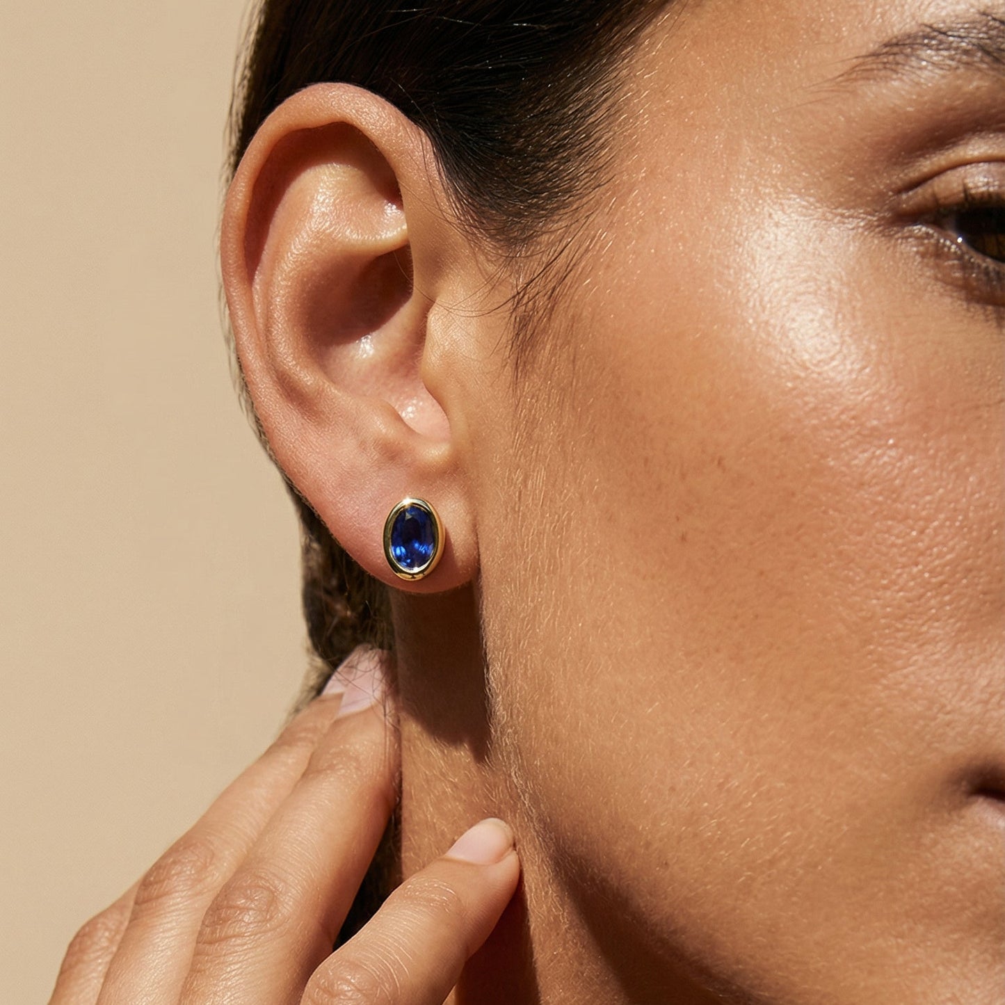 a close up imge of the model wearing blue sapphire yellow gold oval studs 