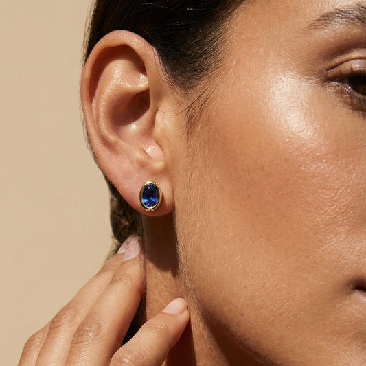a close up imge of the model wearing blue sapphire yellow gold oval studs 