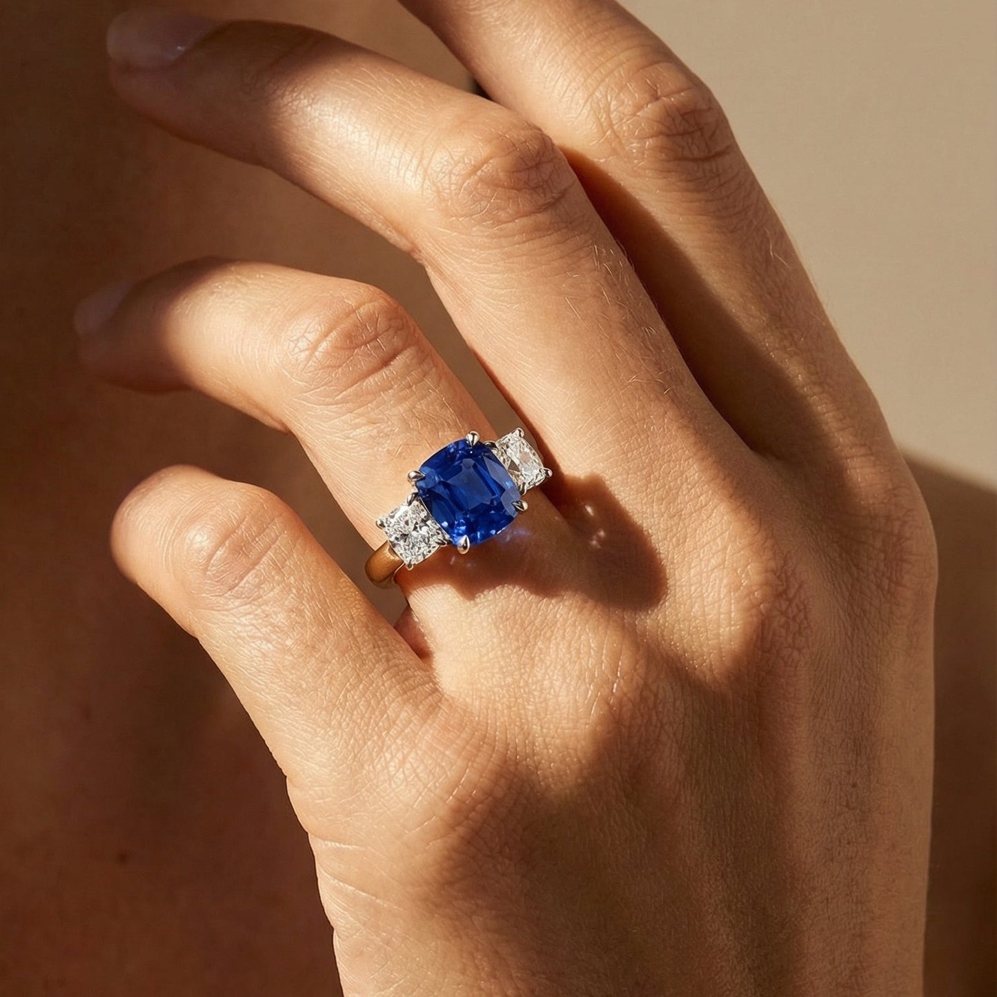 close up image of the models hand wearing a blue sapphire diamond ring in yellow gold 