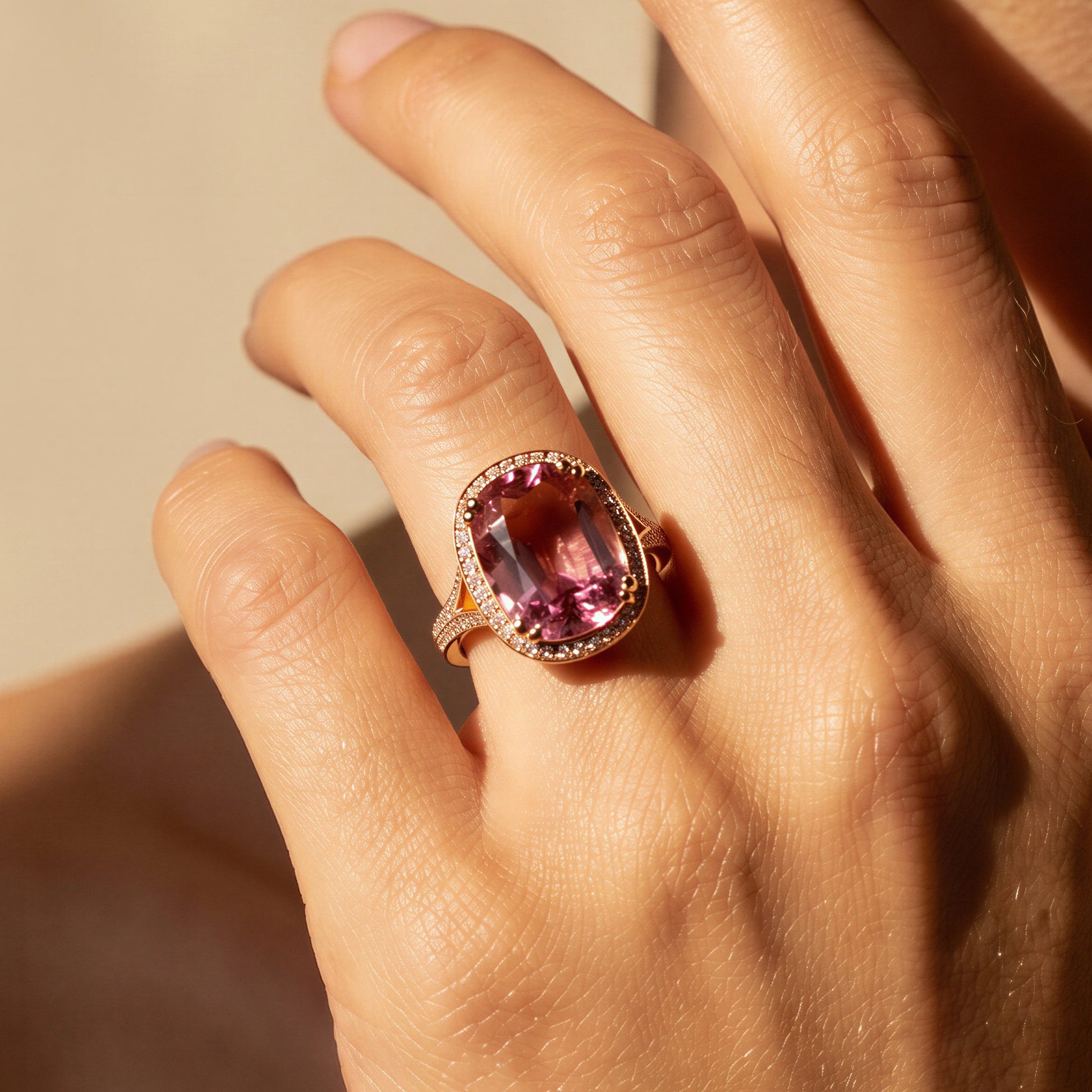 Close-up of a hand wearing a ring with a pink tourmaline gemstone against a neutral background