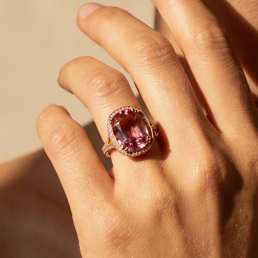 Close-up of a hand wearing a ring with a pink tourmaline gemstone against a neutral background