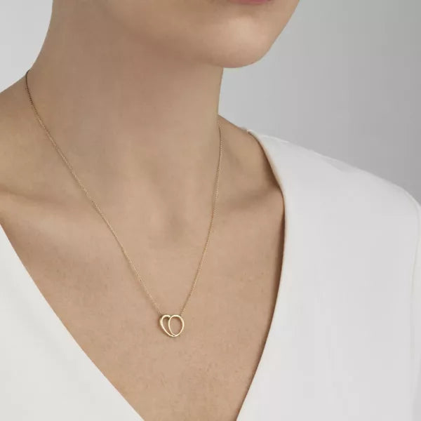 Gold necklace with a heart pendant worn by a person on a plain background