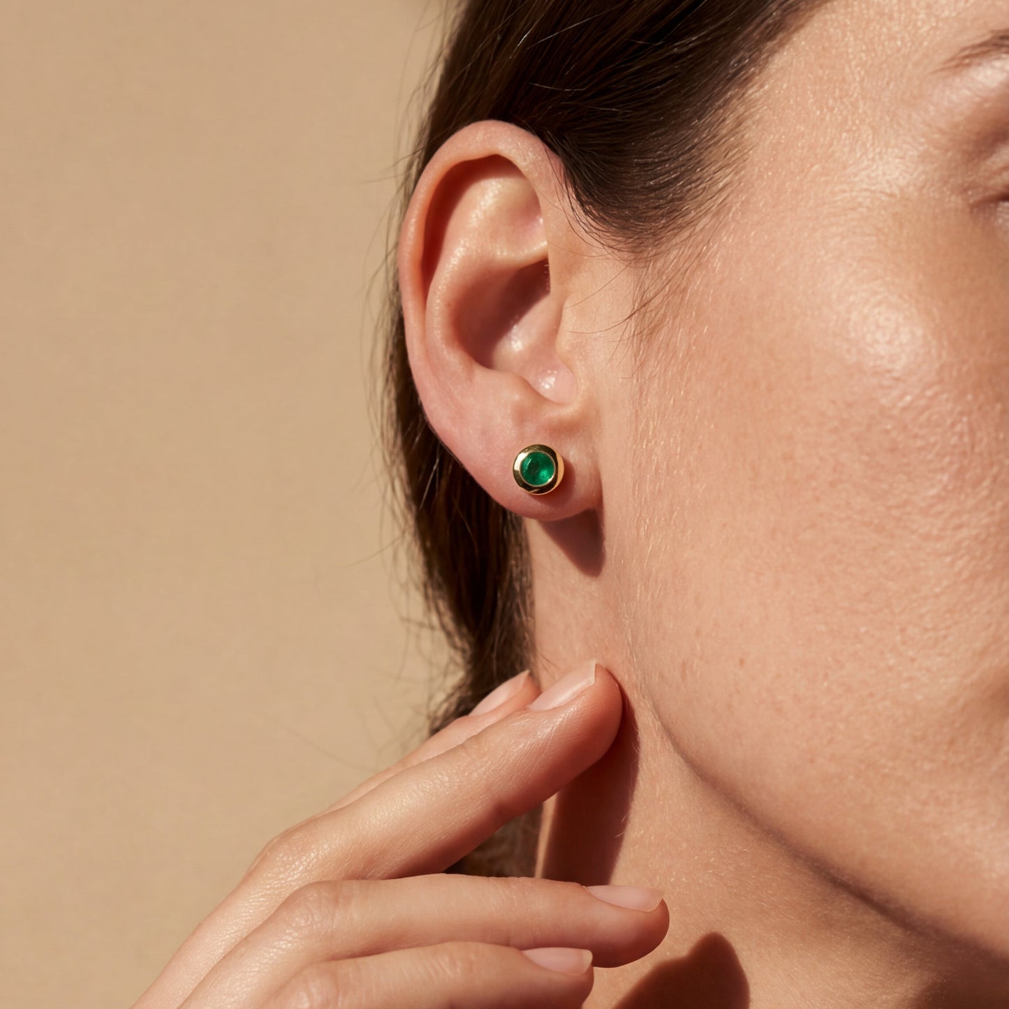 yellow gold green emerald stud earrings worn by a model on a neutral background 