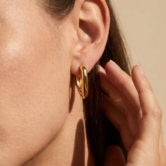 Close-up of a person wearing gold hoop earrings with a neutral background