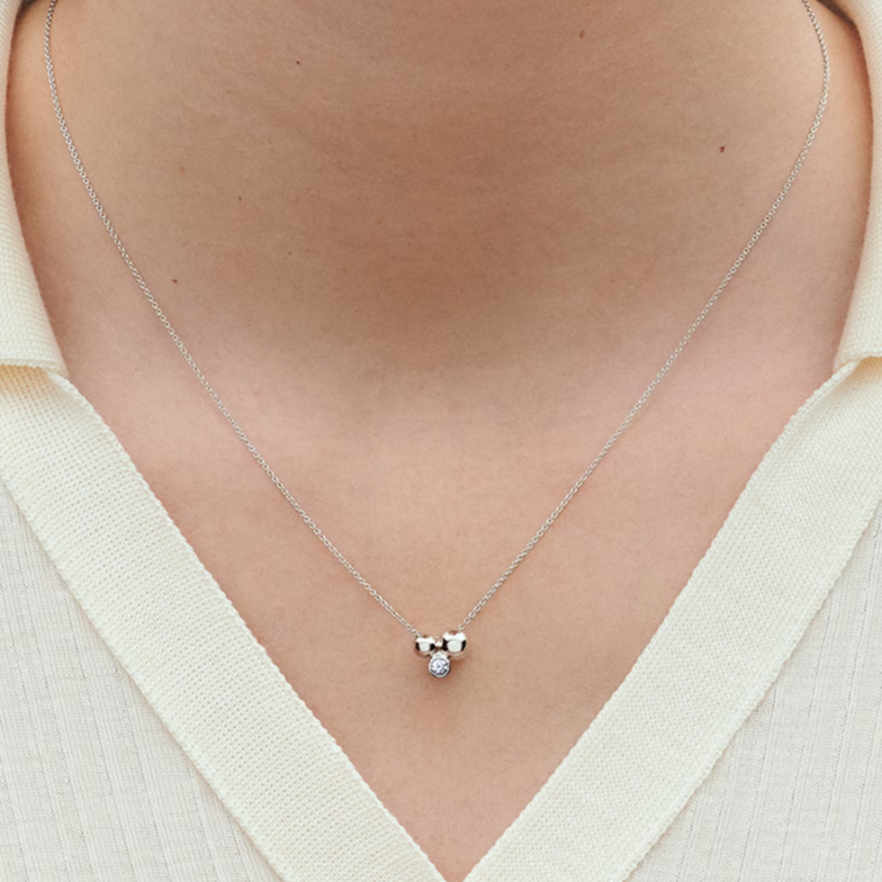 Necklace with a small heart pendant worn by a person in a white shirt.