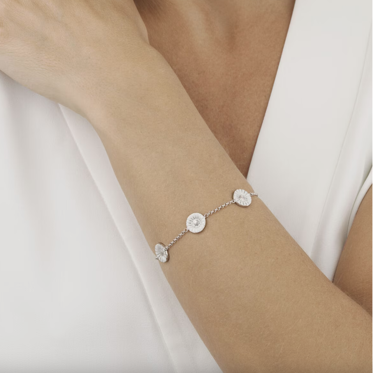 Silver bracelet with floral designs on a wrist against a neutral background