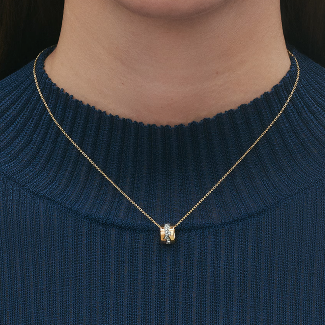 Gold necklace with a pendant on a person wearing a dark blue sweater.