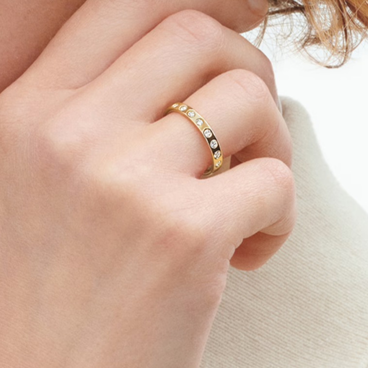 Close-up of a hand wearing a gold ring with small stones on a neutral background