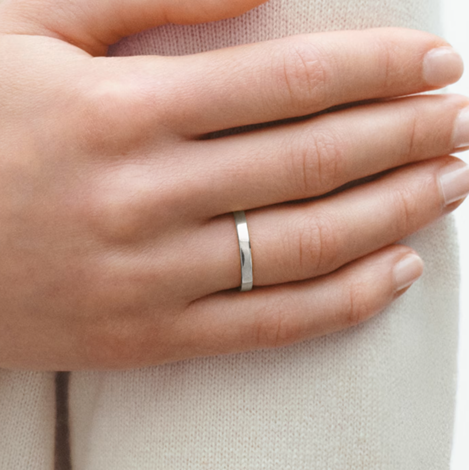 Hand wearing a white gold ring on a neutral background
