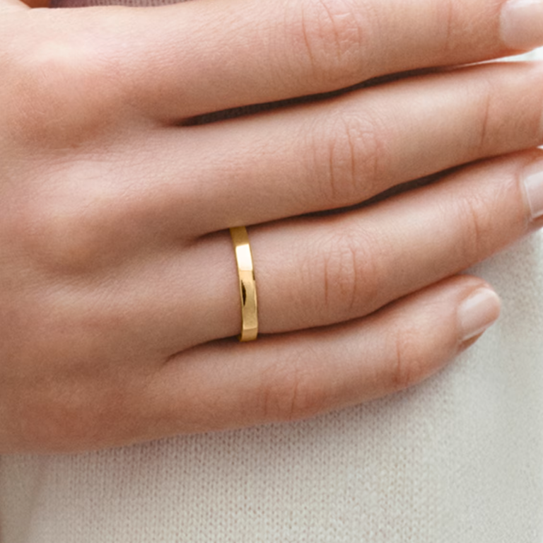 Gold ring on a person's finger against a neutral background