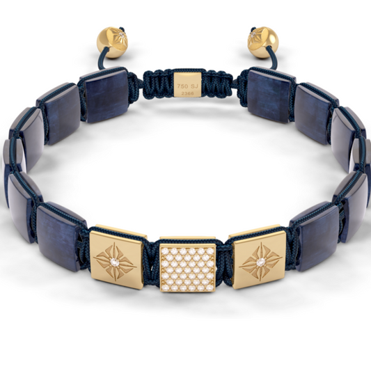 A bracelet by Piaget featuring dark blue square links, two gold-tone compass rose links, one gold link with a diamond-pattern center, and a dark blue cord adjustable closure with gold beads.