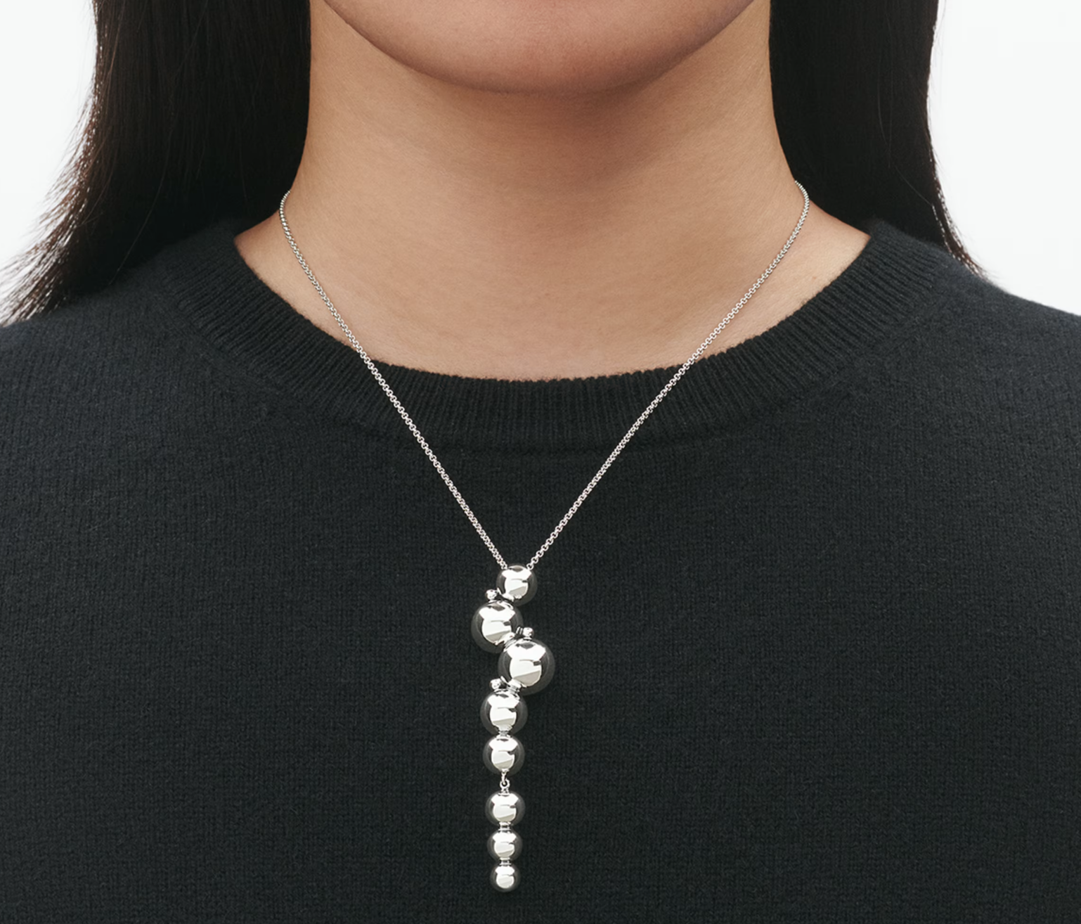 Silver necklace with a pendant worn by a person against a black background