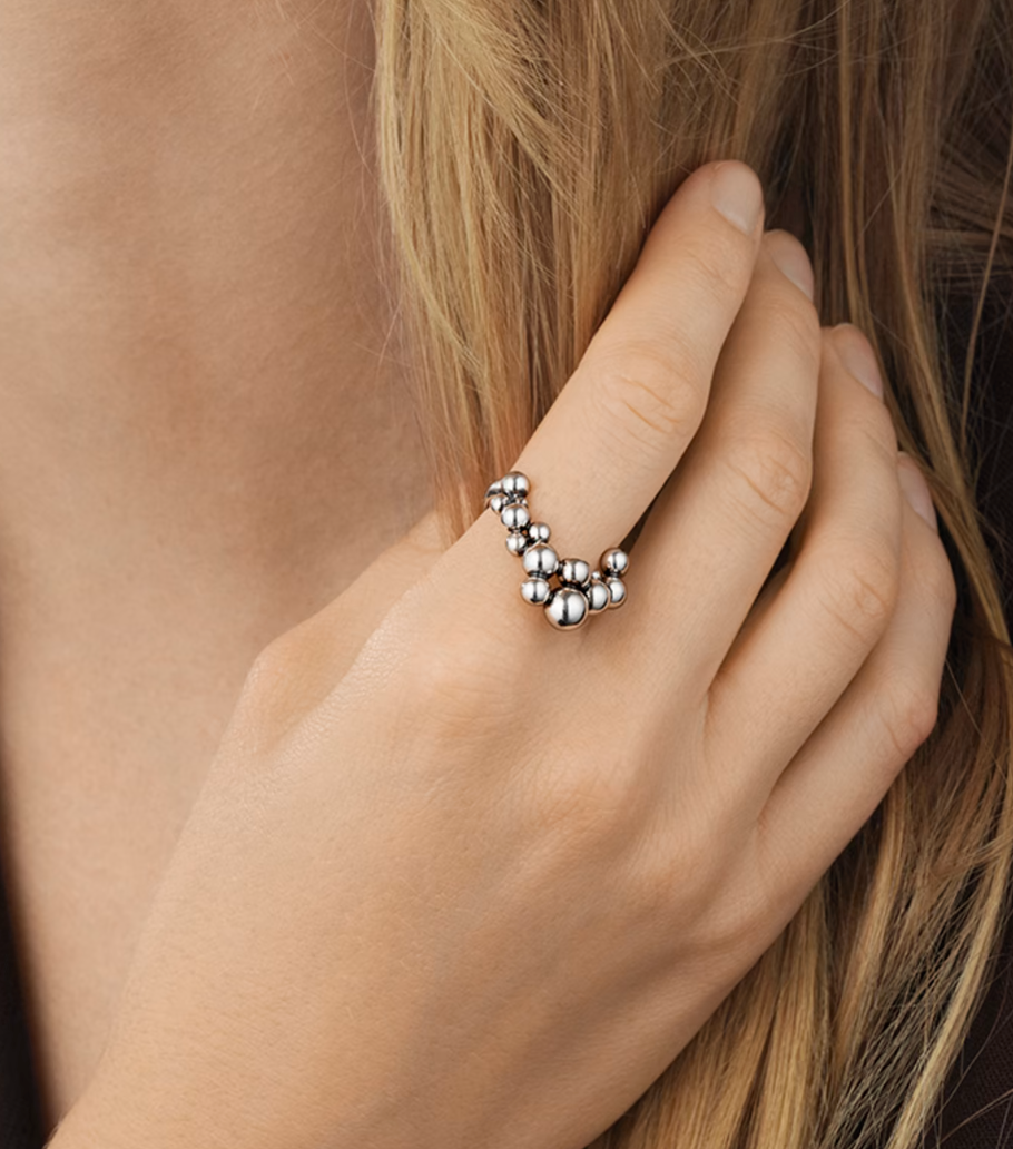 Silver ring with beads worn on a finger against a neutral background