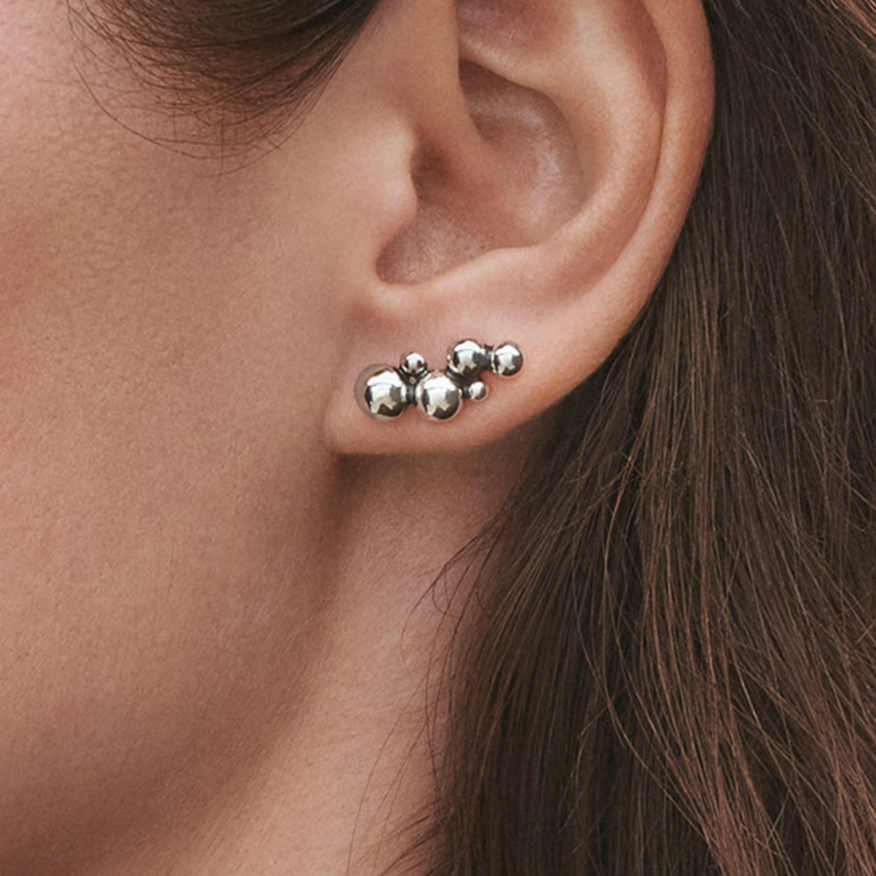 Close-up of an ear wearing silver stud earrings with a blurred background