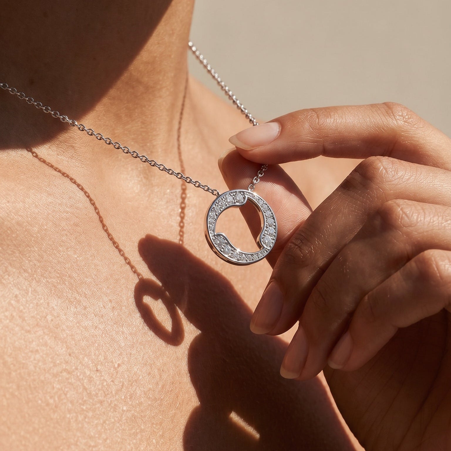 Necklace with a circular pendant held by a hand against a neutral background