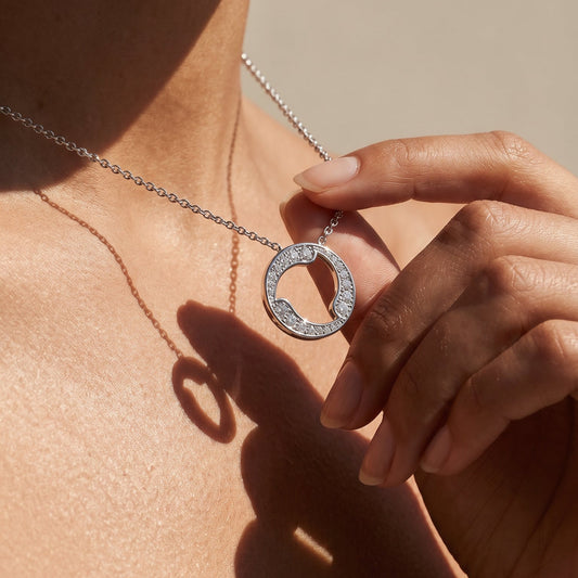 Necklace with a circular pendant held by a hand against a neutral background